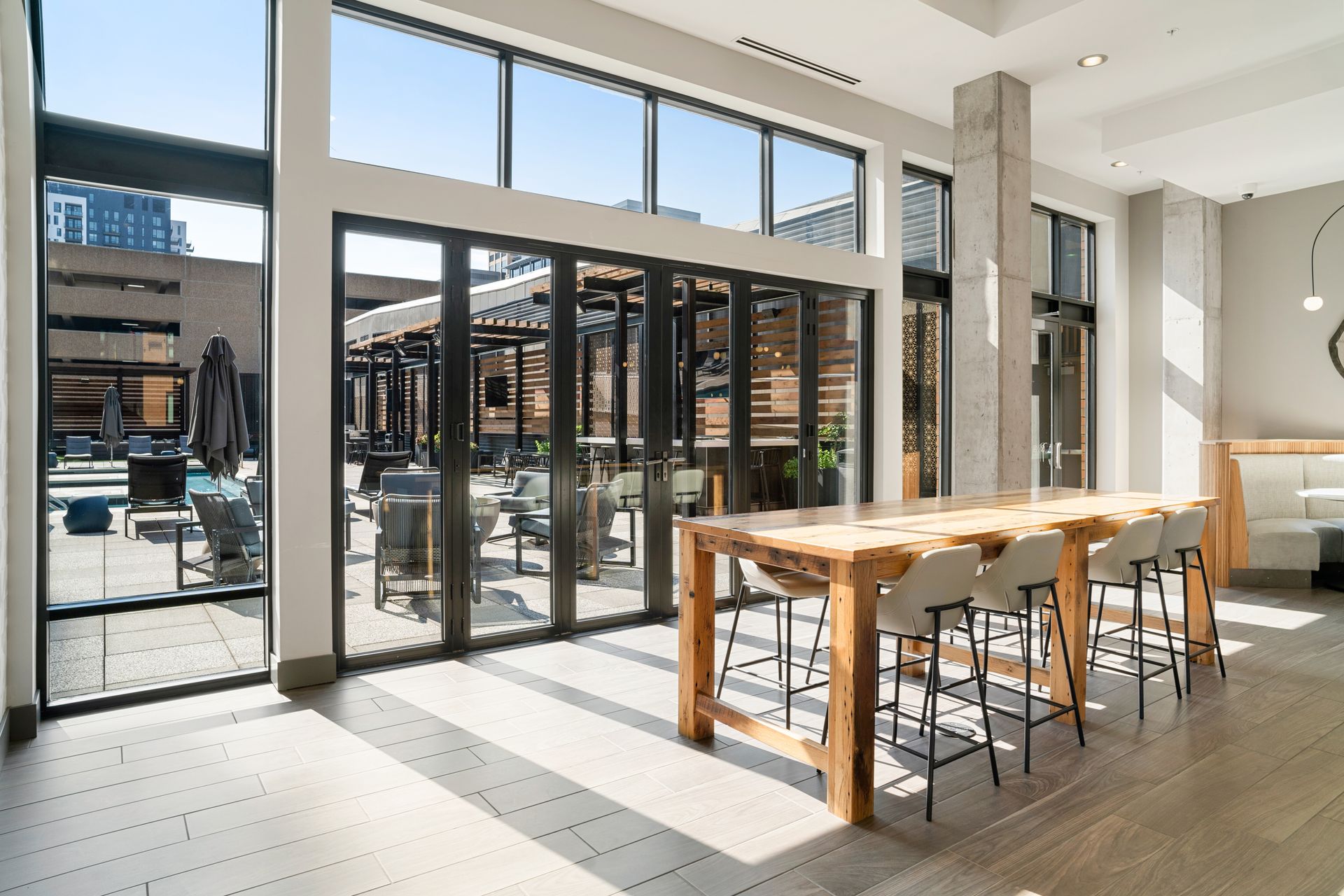Interior with large windows, wooden table, chairs, and patio seating visible outside.