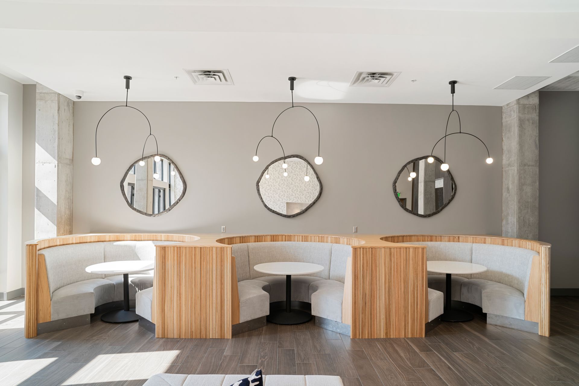 Booth seating in a modern cafe with round mirrors, hanging lights, and light wood and grey tones.