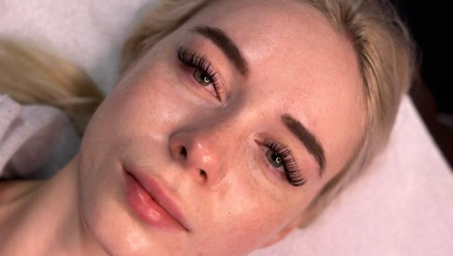 Woman with blonde hair and full eyelashes, lying down, looking at the camera. Soft focus.
