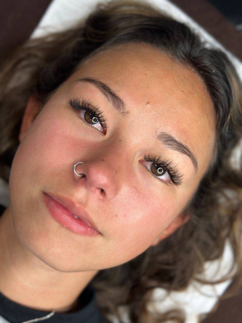 Woman with dark eye makeup, nose ring, and dotted eyeliner, looking up, laying down.