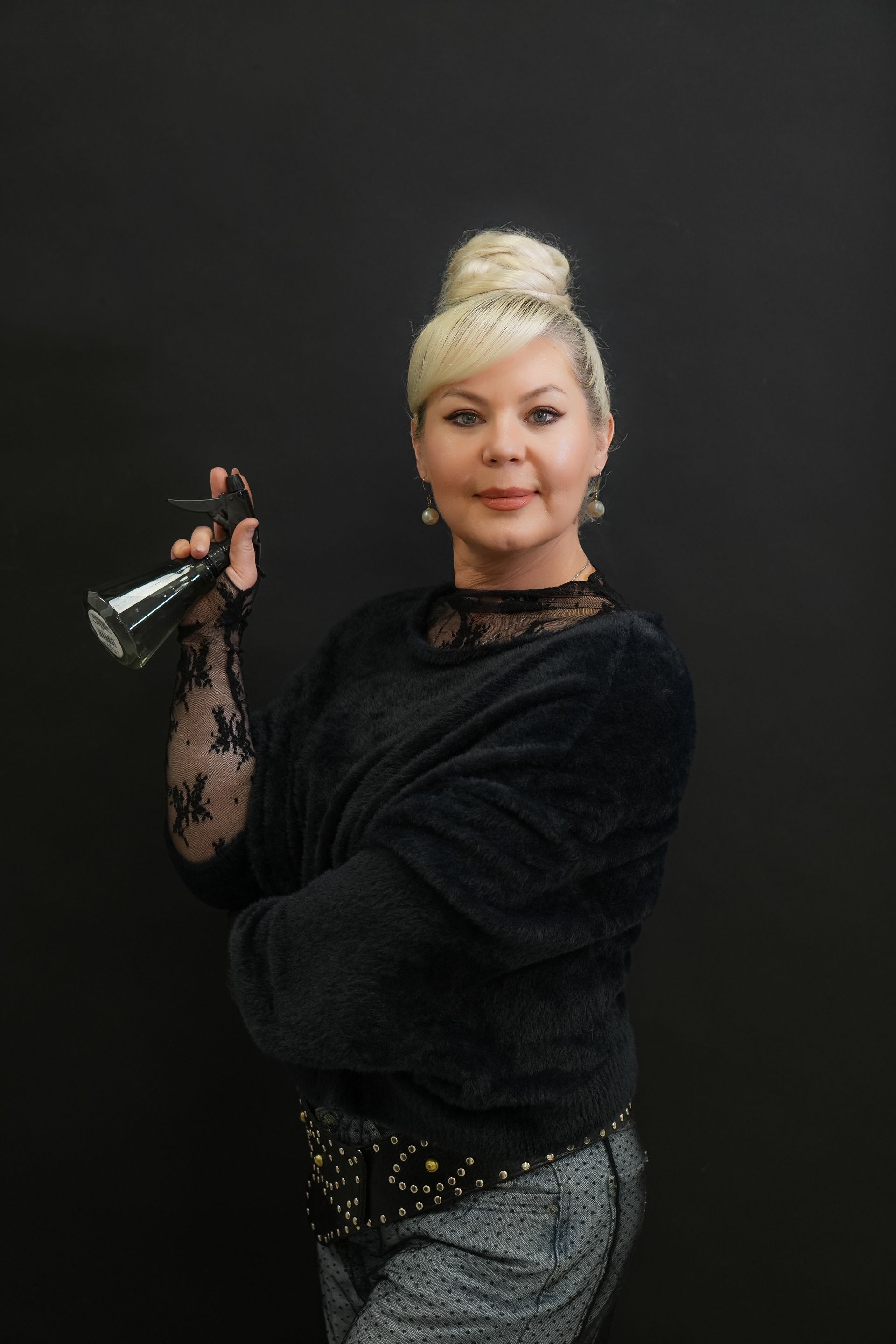 Woman with wavy blonde hair, wearing a black shirt, smiles against a gray background.