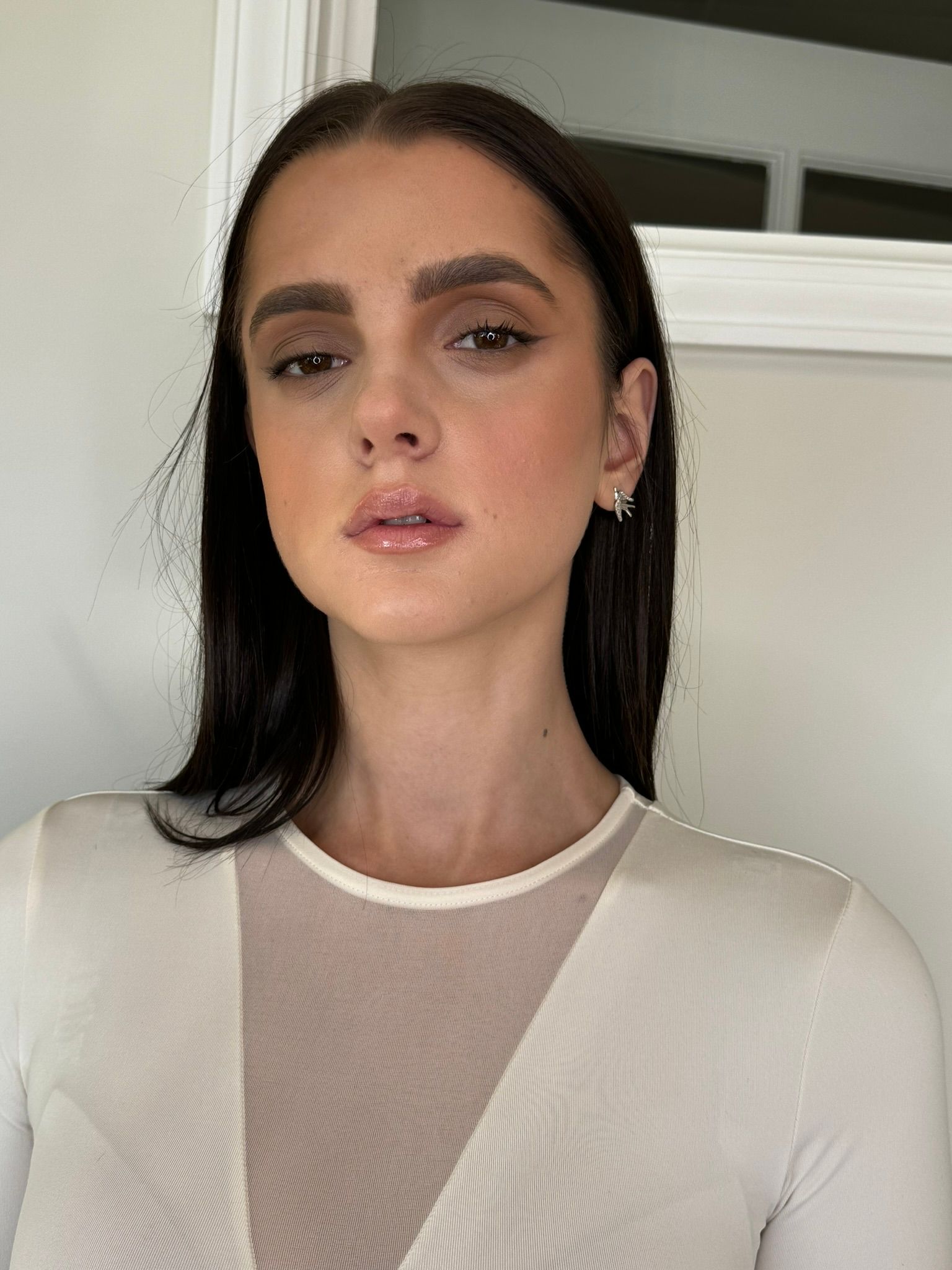 Woman with dark hair and light skin wearing a white mesh top, looking towards the camera.