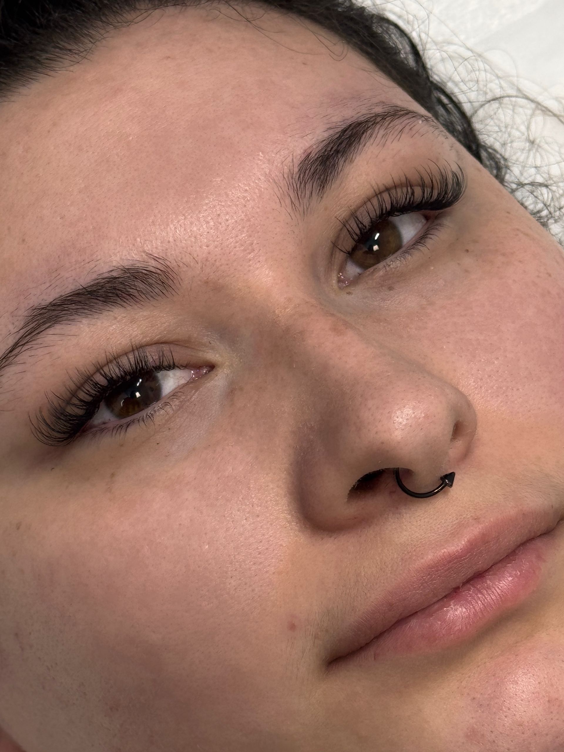 Woman with dotted eyebrows and eyeliner, nose ring. Close-up of face.