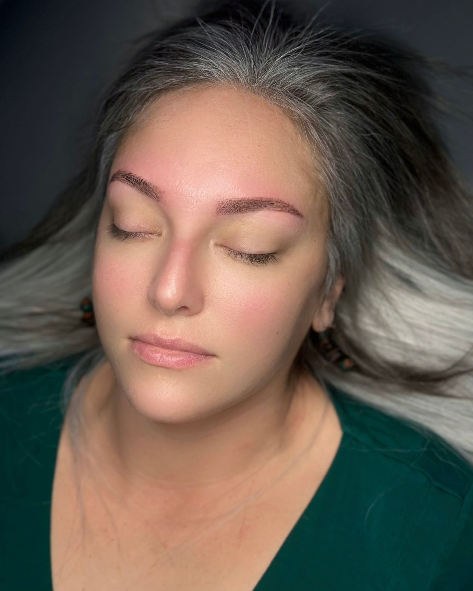 Woman with closed eyes, fresh eyebrow microblading, pale pink.