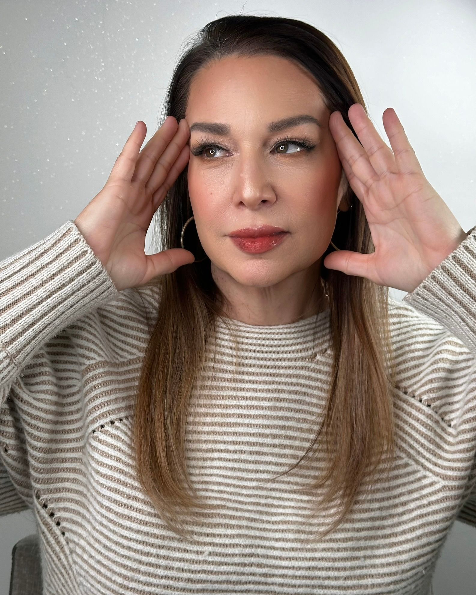 Woman with hands on head, looking to the side, wearing a striped sweater.