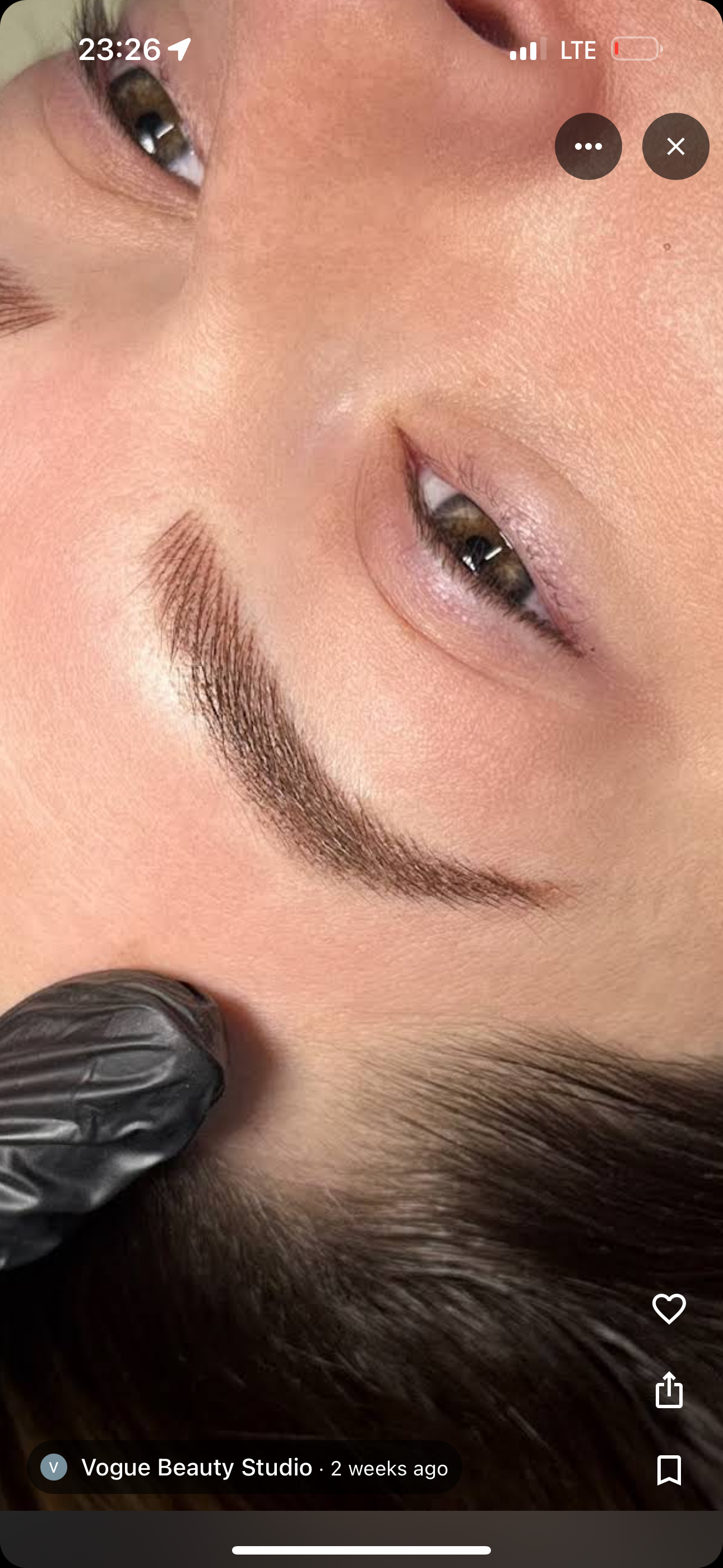 Close-up of a person's eye, with a dark, newly shaped eyebrow. Black glove is visible in the corner.