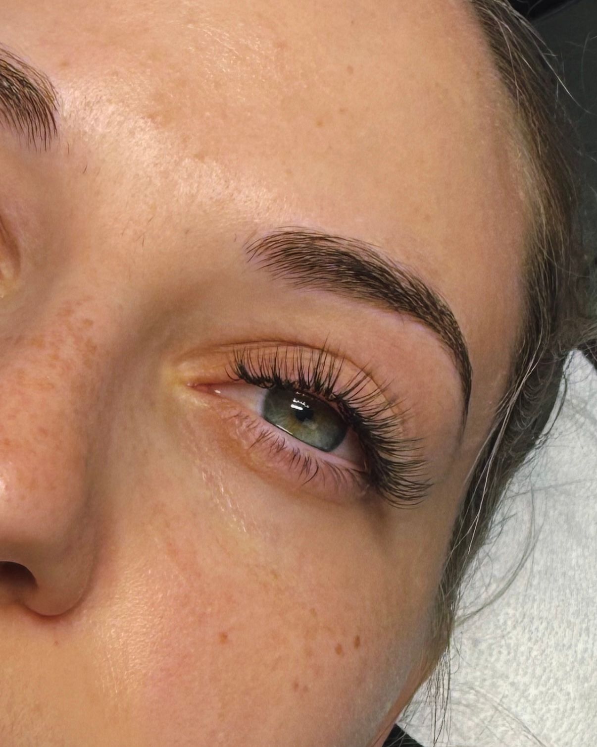 Close-up of eye with dark eyelashes and filled-in eyebrow. Fair skin, green eye, and freckles.