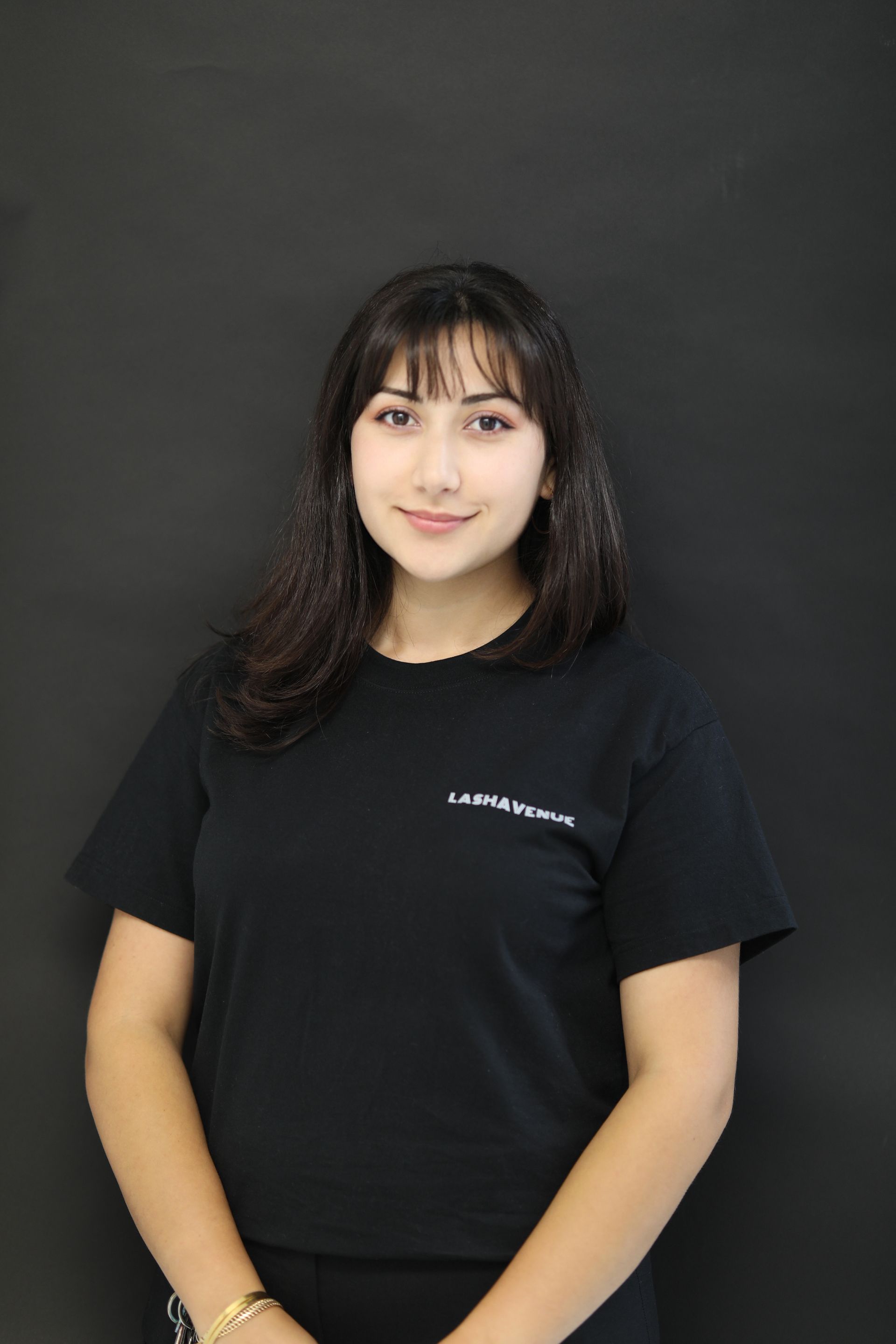 Woman in black shirt, dark hair, smiling, in front of a dark backdrop.