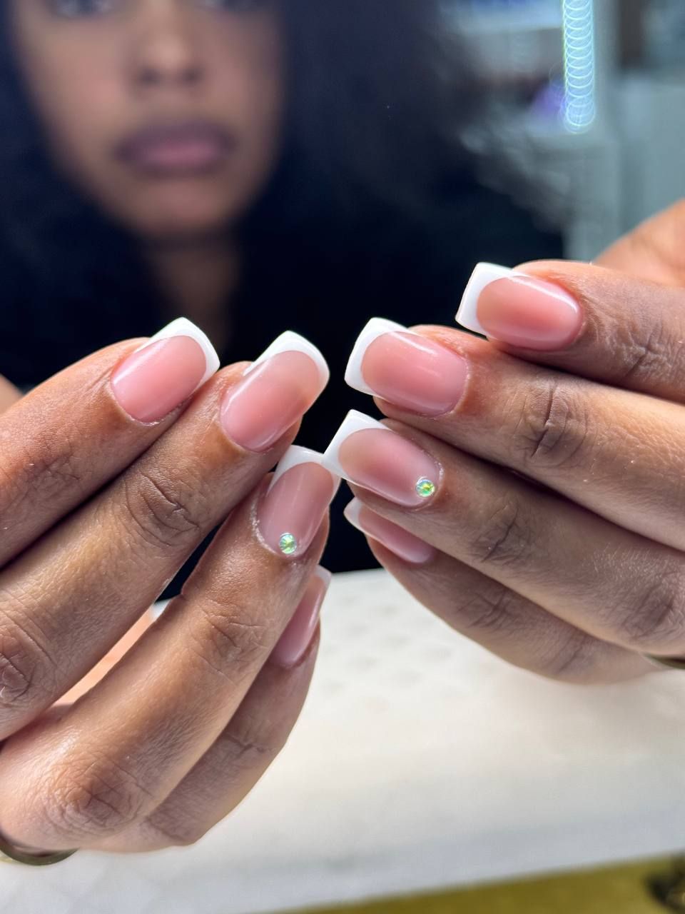 Hands with French tip nails, pink base, and small rhinestones.