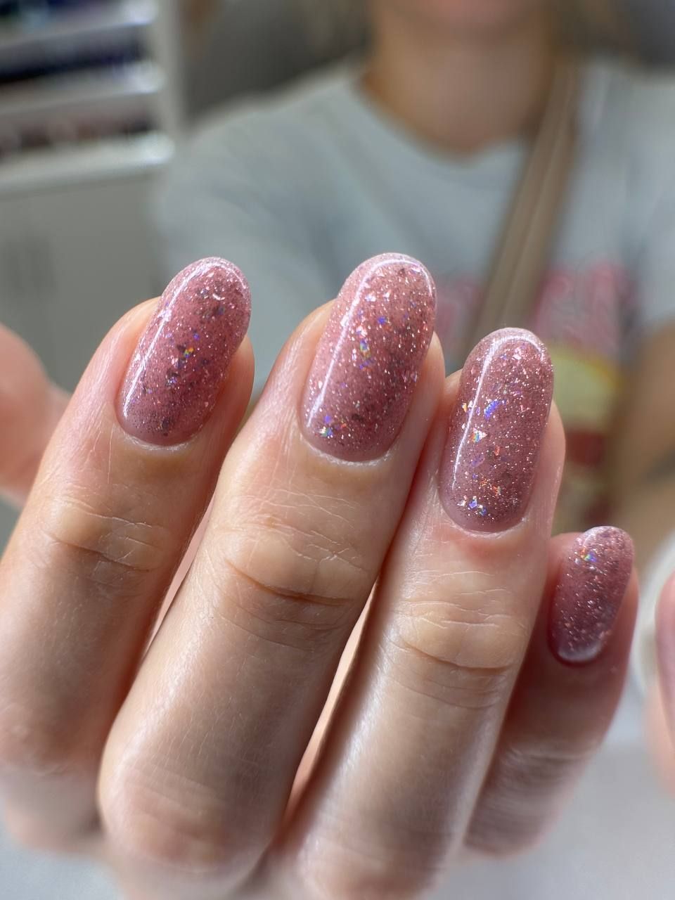 Pink glitter gel nails on a hand, in a well-lit setting.