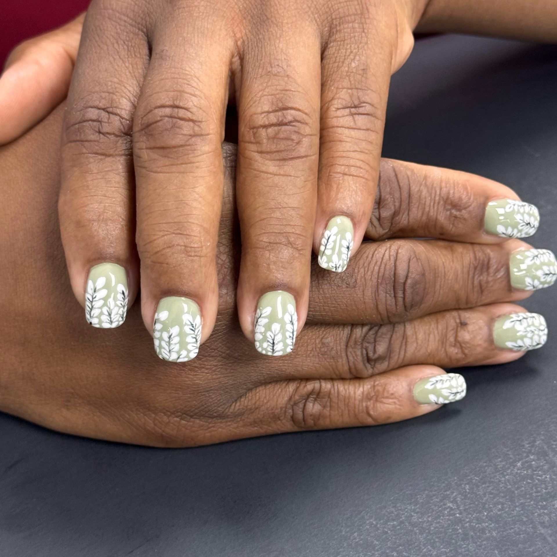 Hands with olive-green nails decorated with white floral patterns.