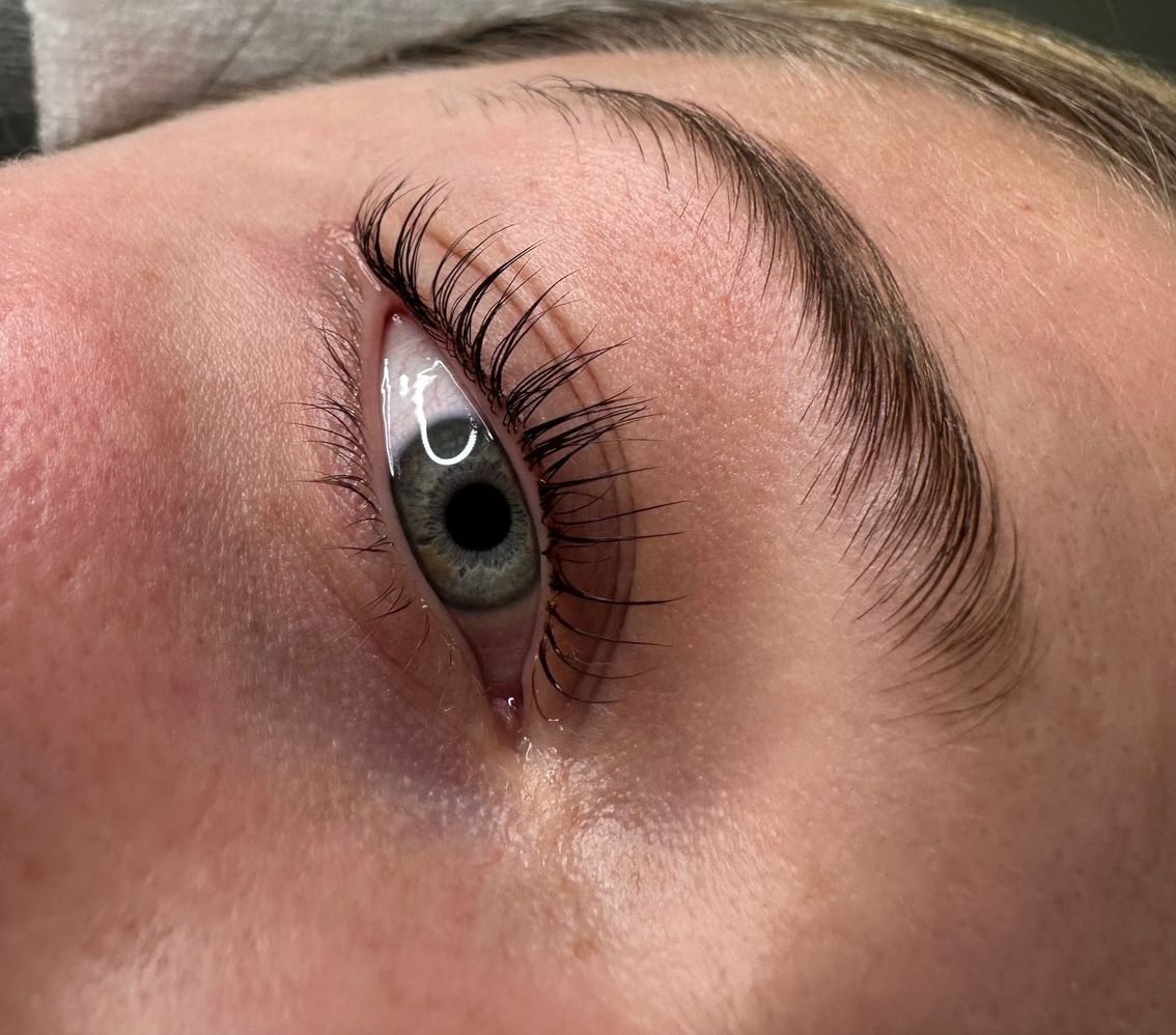 Close-up of an eye with curled, dark lashes and well-groomed eyebrow. The eye is open and the skin is pale.