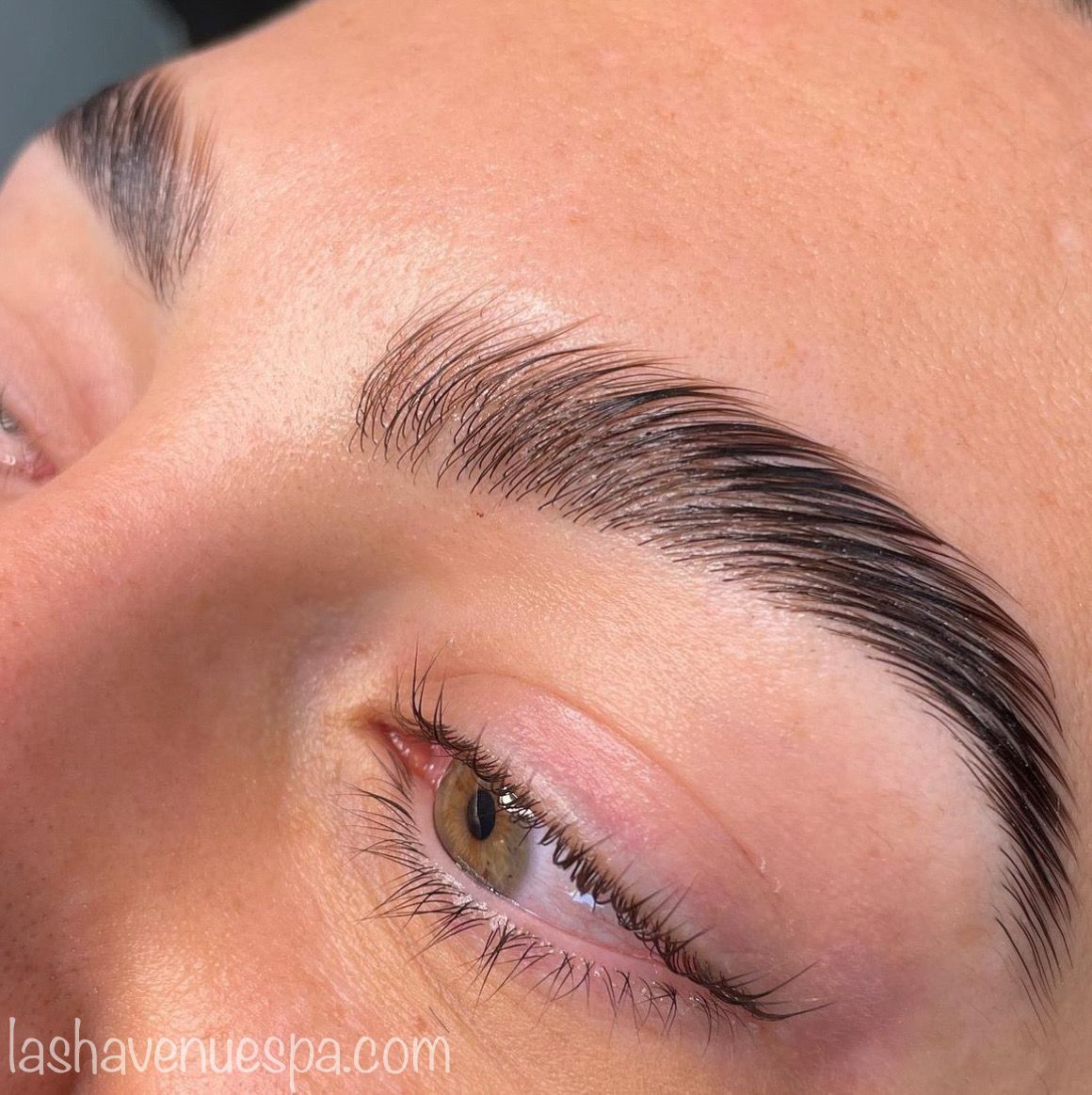 Close-up of a person's eye and eyebrow after a brow lamination treatment, showcasing lifted, glossy hairs.