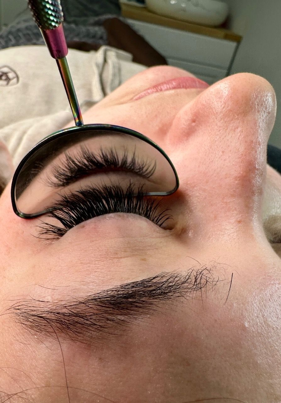 Close-up of eye with lash extensions, being checked with a curved mirror during a beauty treatment.