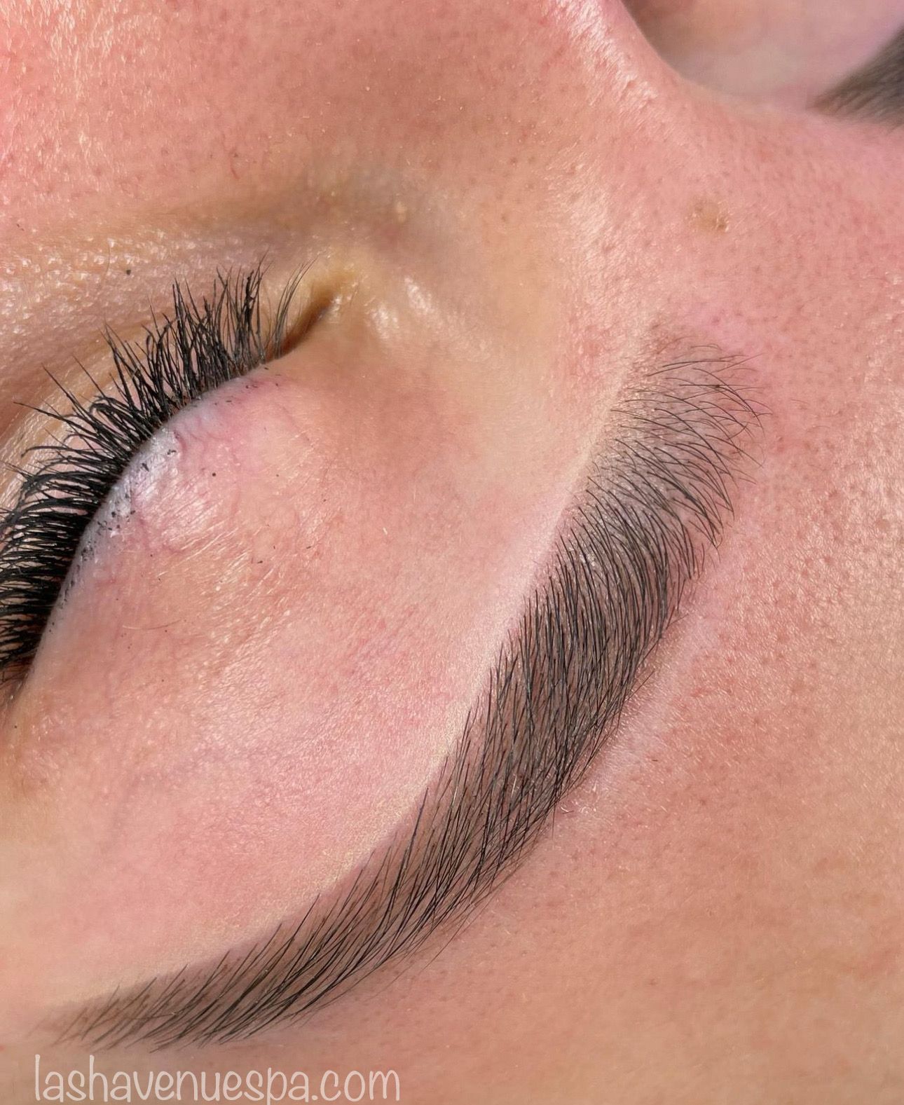 Close-up of an eyebrow with a filled-in, dark color and the closed eye of a person with long eyelashes.