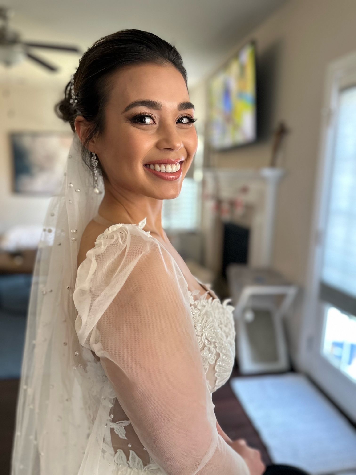 Bride in wedding dress, smiling, with veil and updo, indoors.