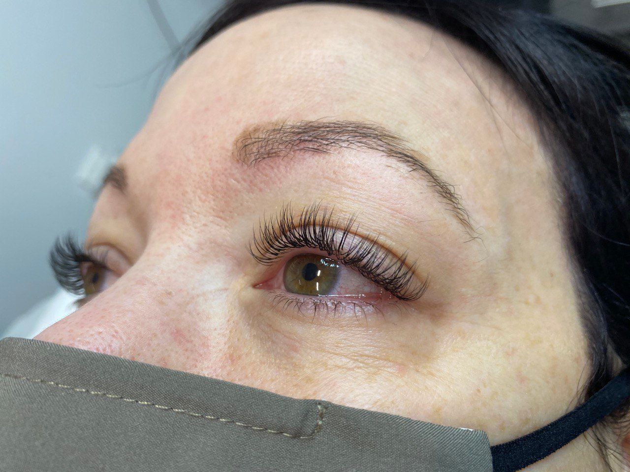 Close-up of a person's eye with semi-permanent makeup on eyebrows and eyeliner, wearing a mask.
