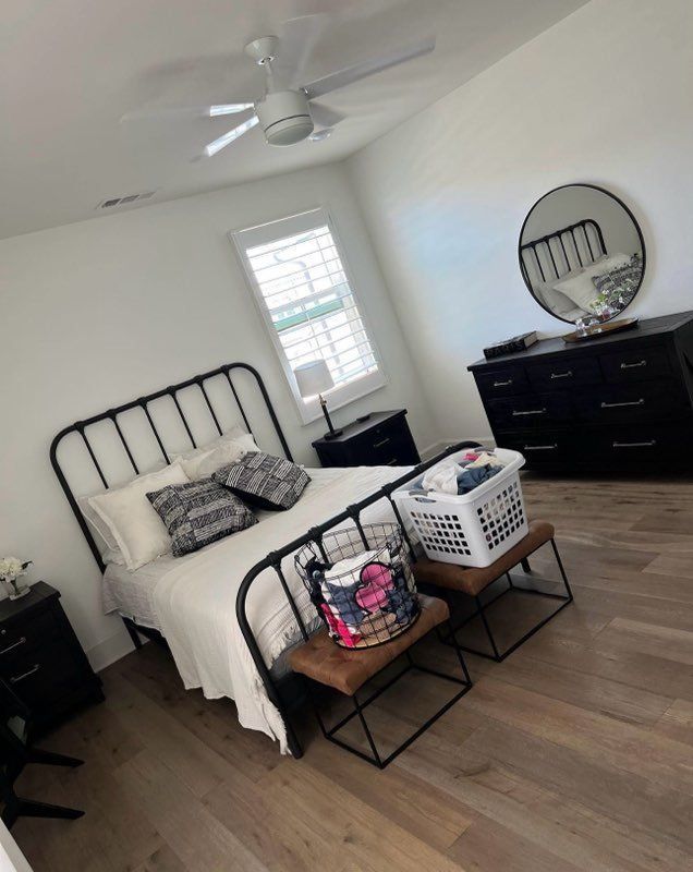 Bedroom with black metal bed frame, black dresser, wooden floor, and a white ceiling fan.