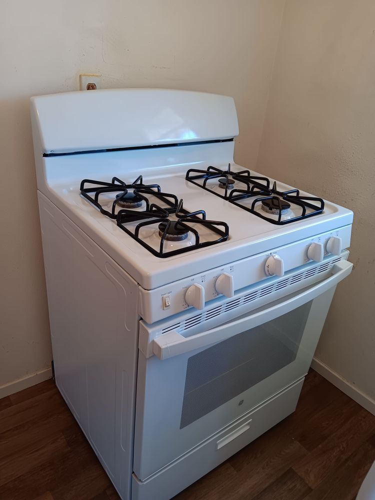 White gas range with four burners and oven, in a kitchen corner.