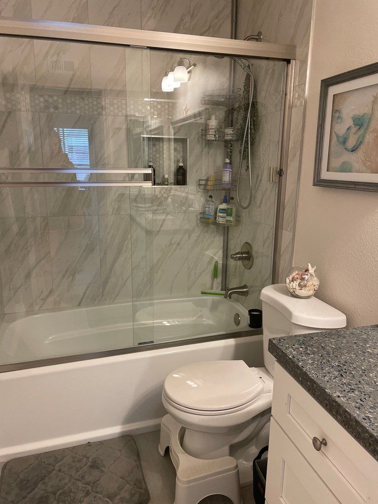 Bathroom with white tub, toilet, glass shower doors, and marble-look tile.