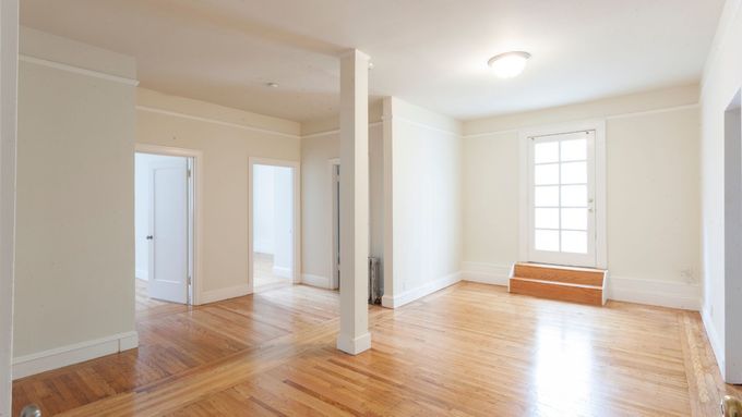 Empty room with hardwood floors, white walls, and a window with steps.