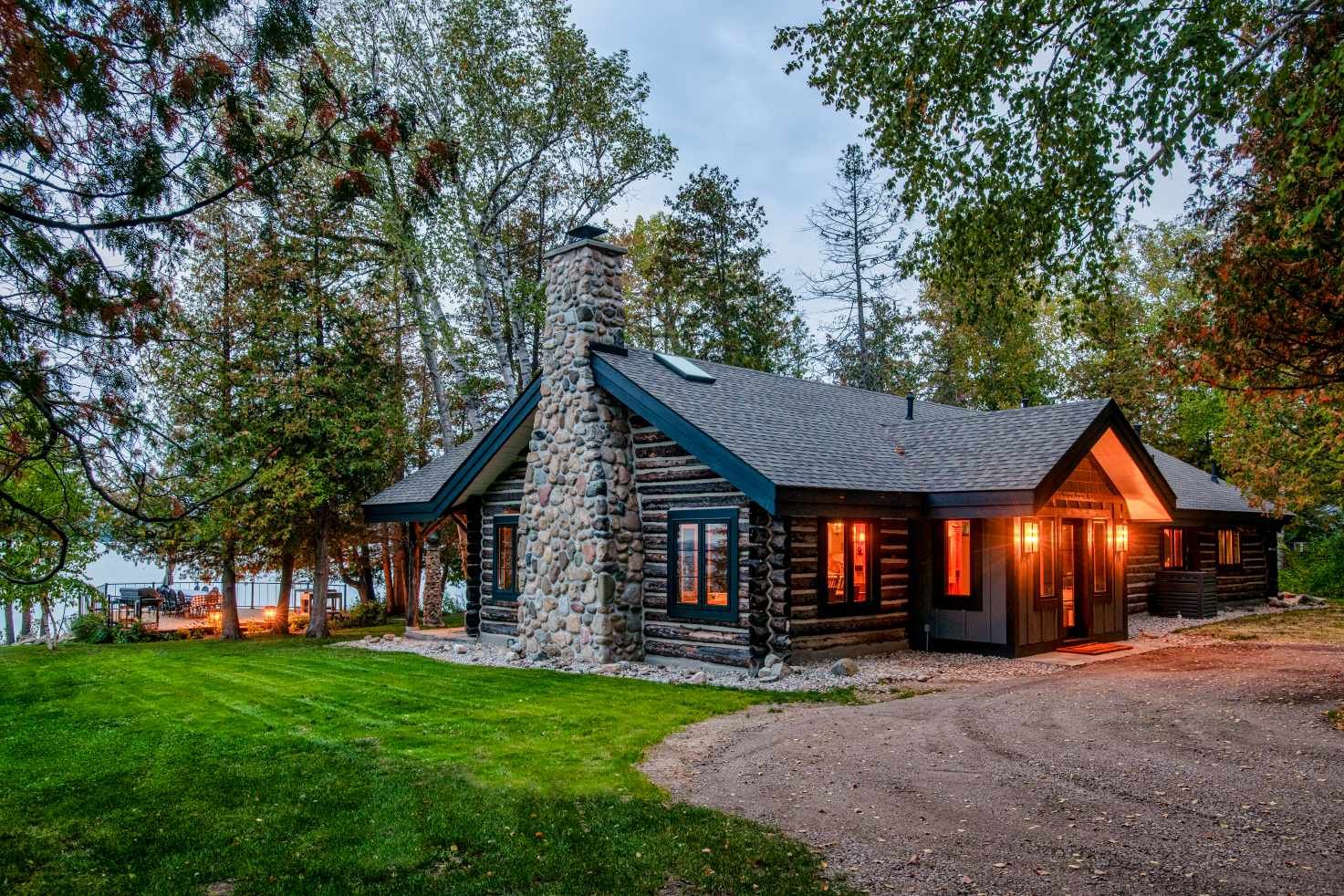 A large log cabin is surrounded by trees and a lake.