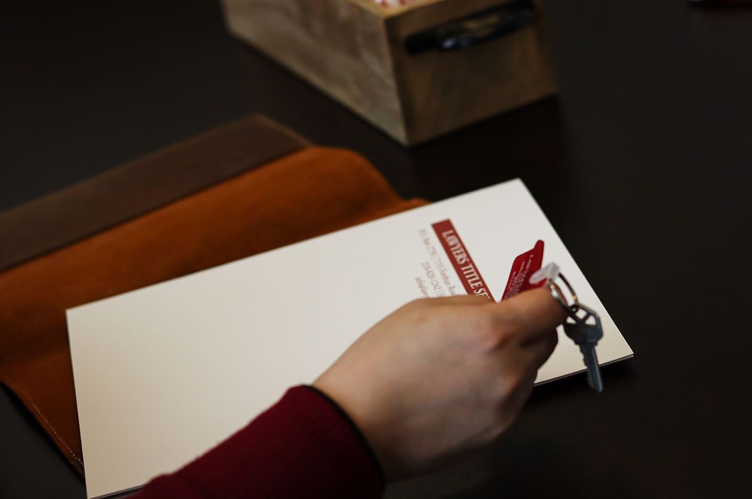 Hand holding keys next to a white card with red text; dark brown leather folio on a dark table.