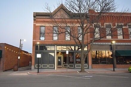 Brick building on a street, storefront windows, leafless tree, evening light.