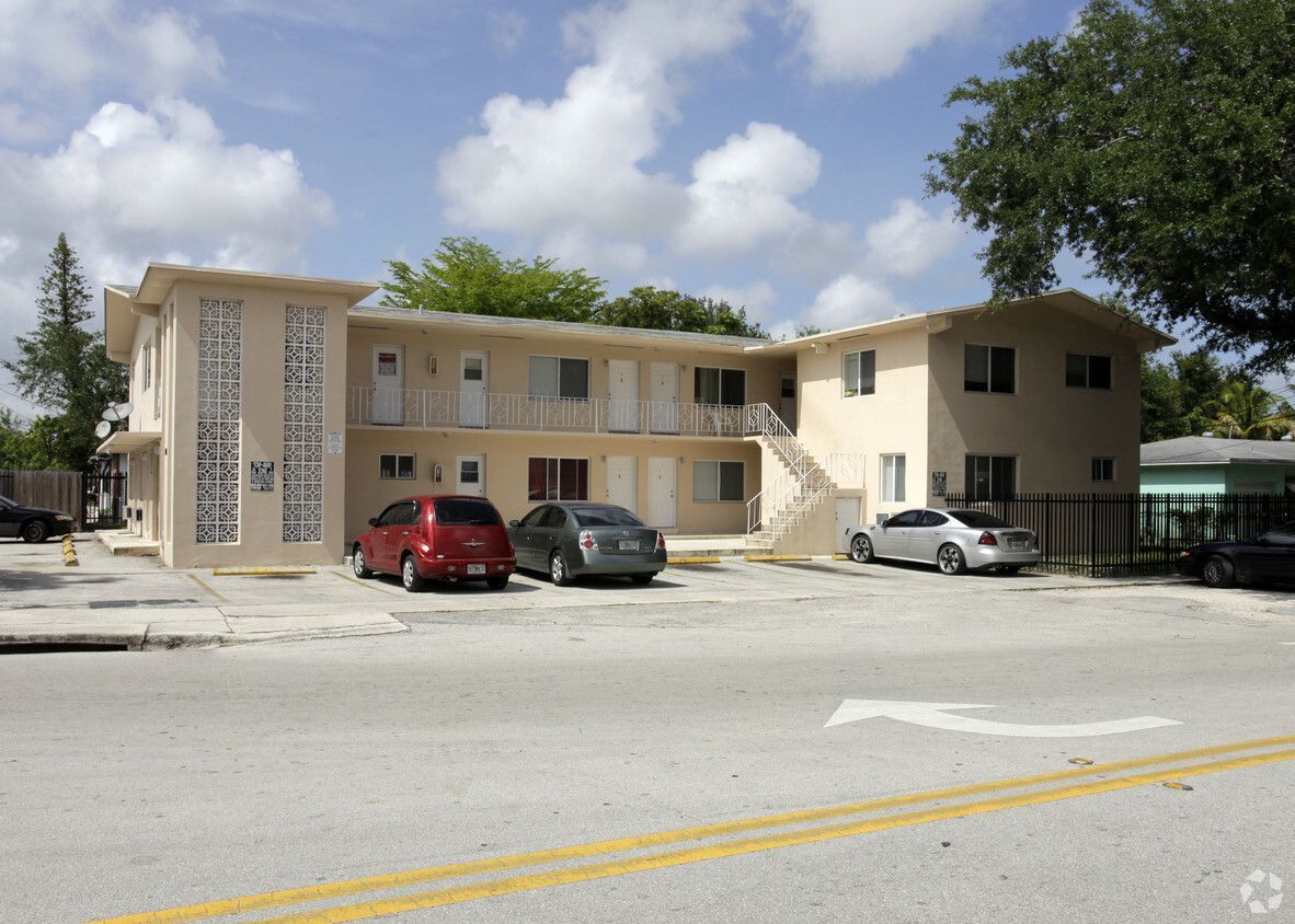 Two-story beige apartment building with cars parked in front on a sunny day.