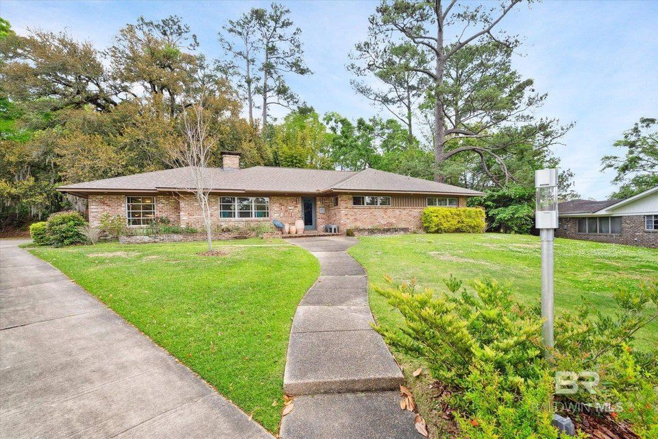 A brick ranch home with a walkway, surrounded by green lawn and trees.