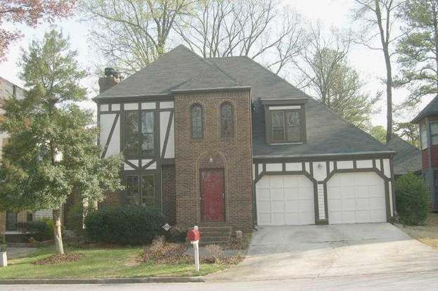 Two-story Tudor-style house with brick and white accents; red door, two-car garage.