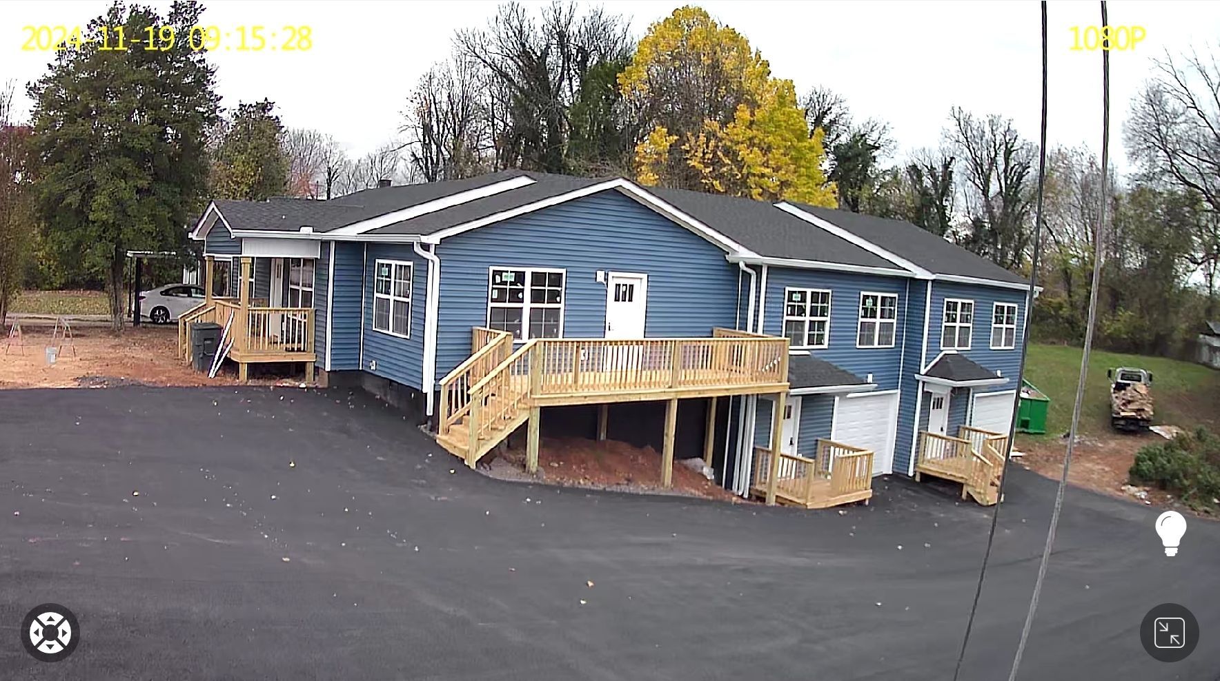 Blue house with wooden decks and a paved driveway on a cloudy day.