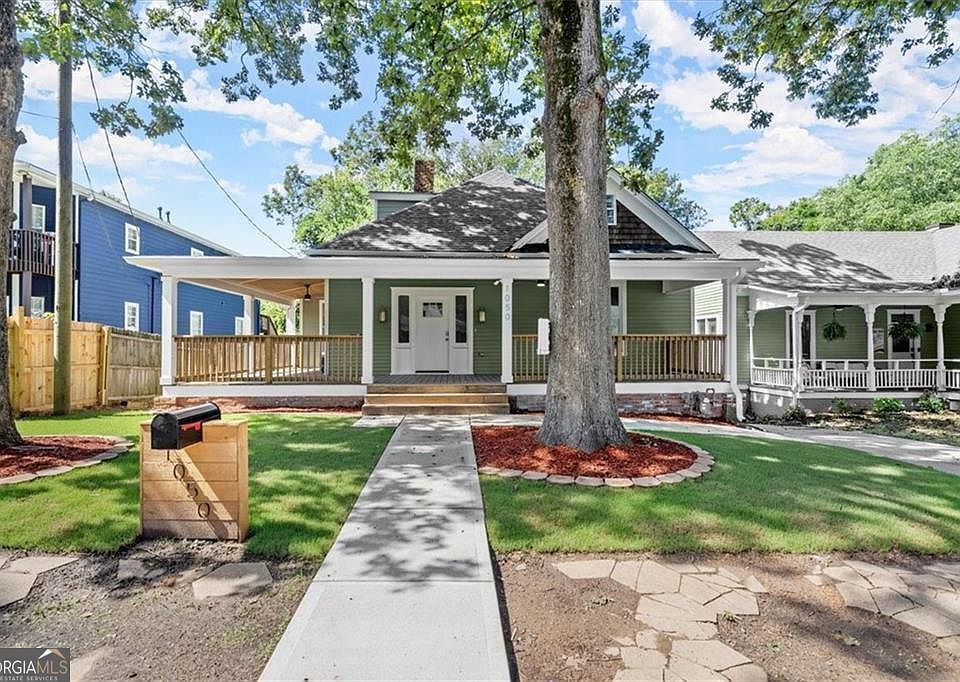 Green house with porch, steps, and mailbox, a tree in front, sunny day.