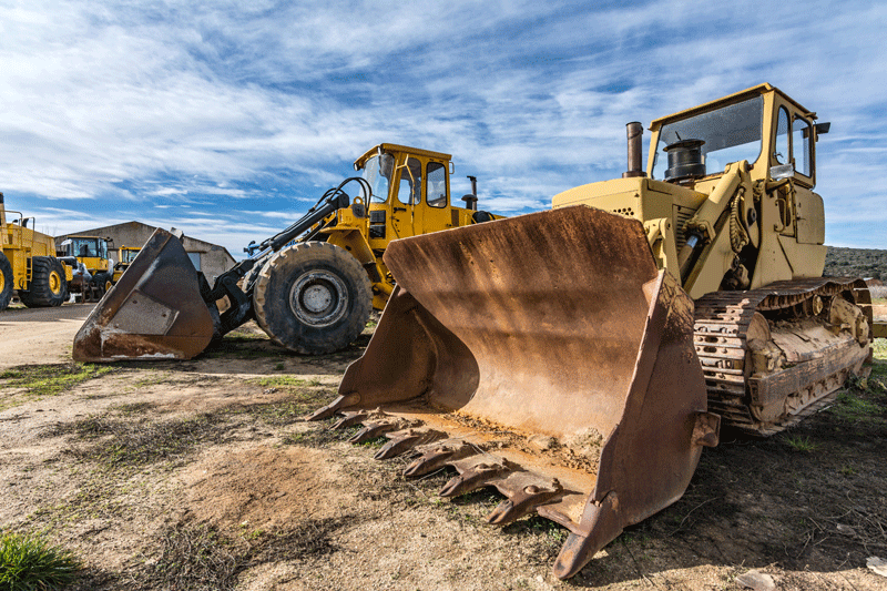 Two Bulldozers Are Parked Next to Each Other in A Dirt Field.