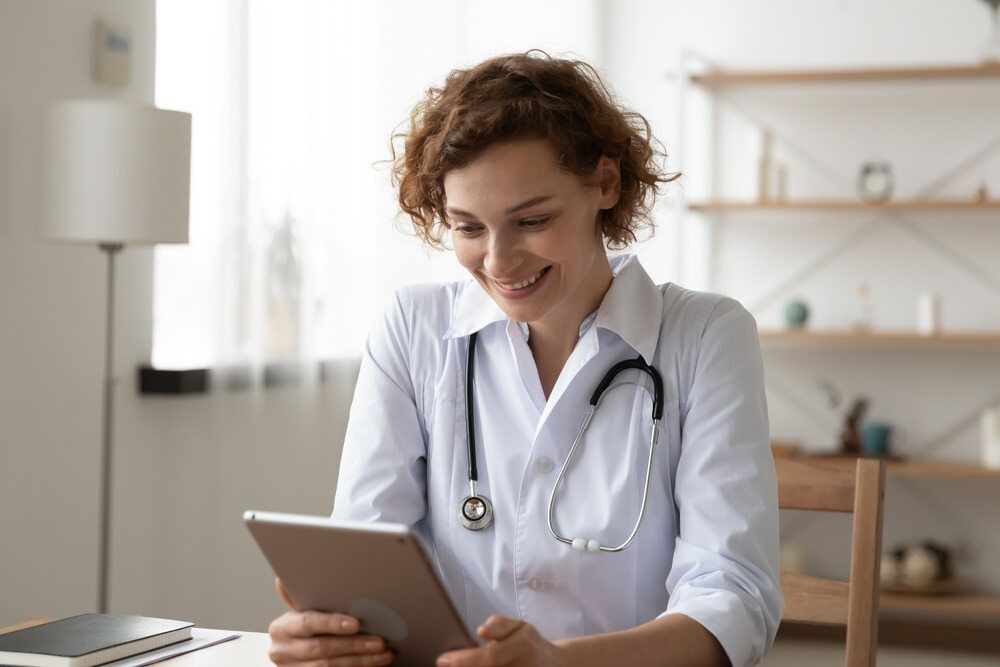 Smiling Doctor With Curly Hair in a White Coat with Stethoscope, in a Bright Room — Tewantin Medical Centre In Tewantin, QLD