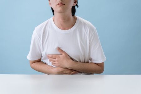 Person in white shirt holds stomach, appearing to be in pain, against a blue background.