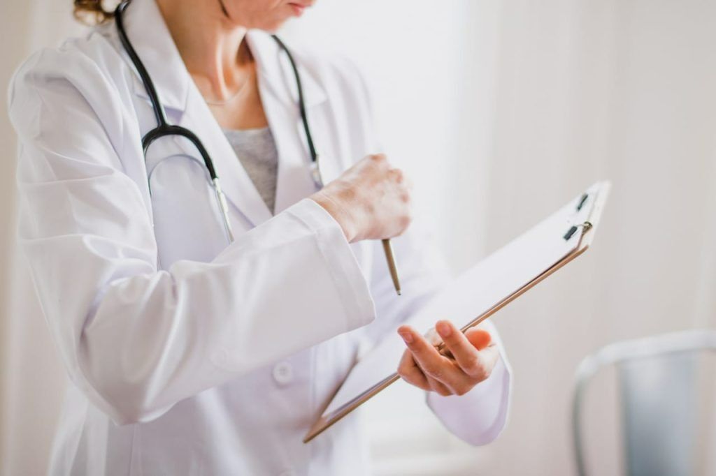 Doctor in White Coat With Stethoscope Holding Clipboard, Writing With Pen — Tewantin Medical Centre In Tewantin, QLD