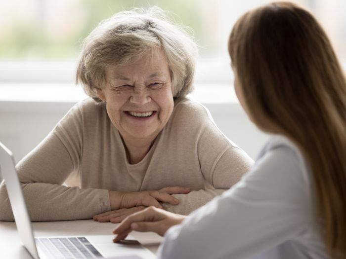 Elderly Woman Smiles While Looking at a Laptop With a Doctor at a Table — Tewantin Medical Centre In Tewantin, QLD