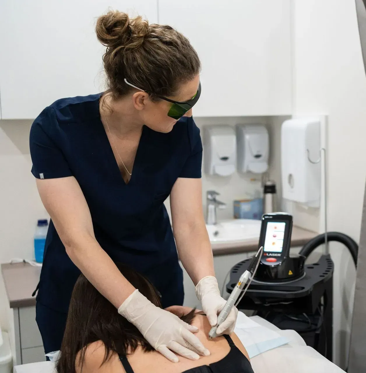 Woman in scrubs operating laser device on another woman's neck, medical setting — Tewantin Medical Centre In Tewantin, QLD