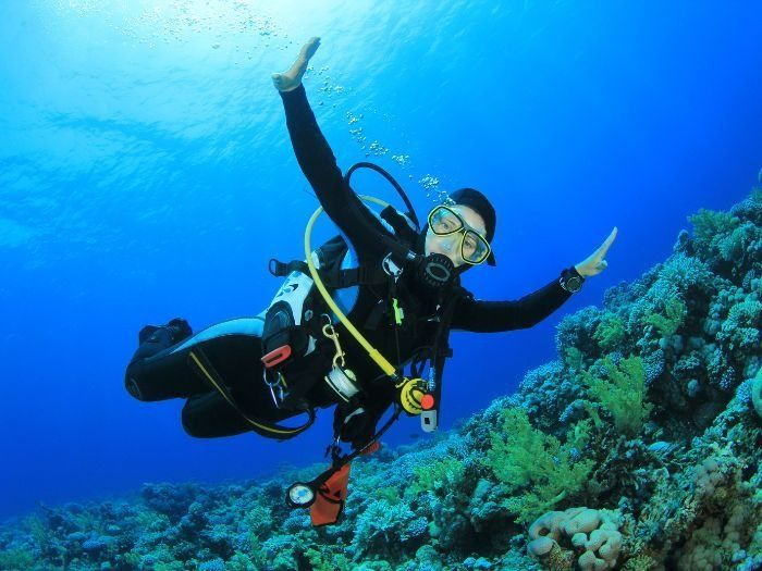 Scuba Diver With Arms Raised, Smiling, in Deep Blue Water Near Coral Reef — Tewantin Medical Centre In Tewantin, QLD