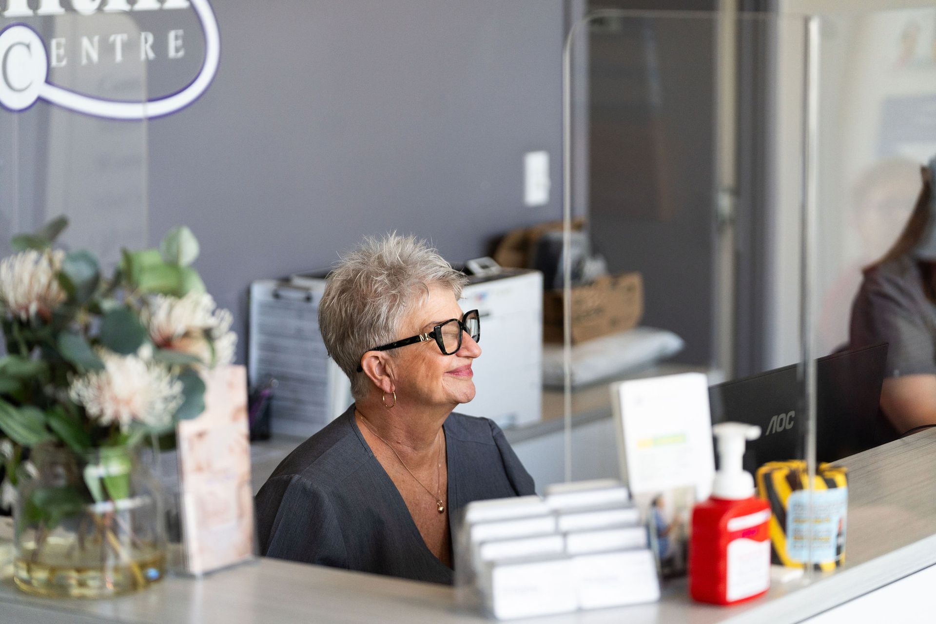 Receptionist smiling behind a clear barrier at a medical center.
