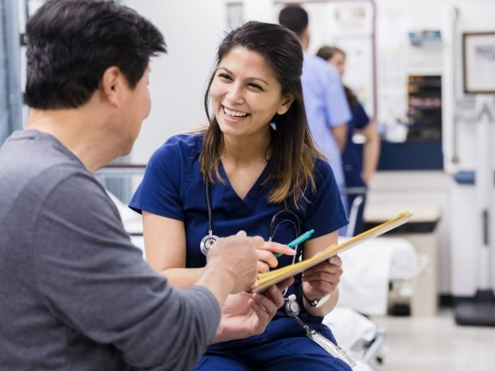 Nurse in Blue Scrubs Smiling, Pointing at a Clipboard While Talking With a Patient — Tewantin Medical Centre In Tewantin, QLD