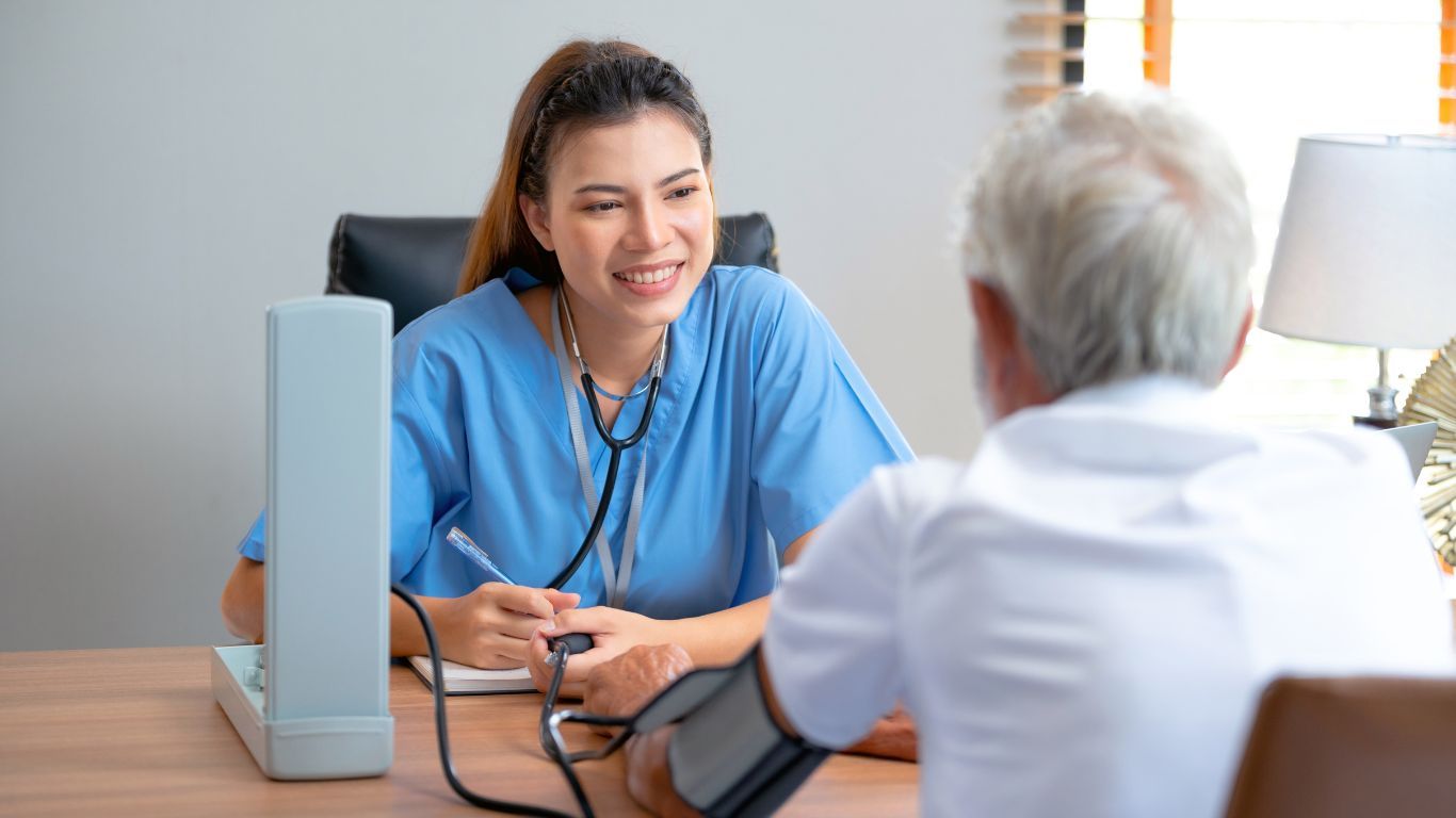Female Nurse Taking an Elderly Man’s Blood Pressure at a Desk in an Office — Tewantin Medical Centre In Tewantin, QLD