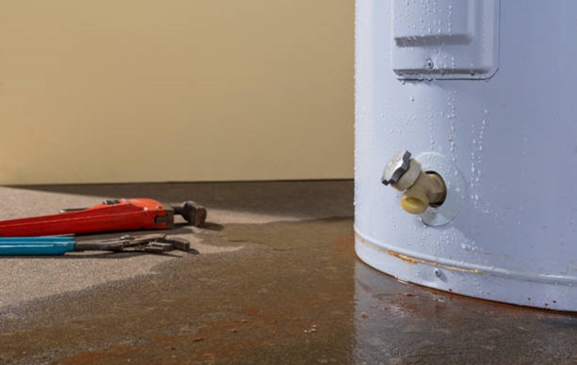 A water heater is sitting on the floor next to a wrench.