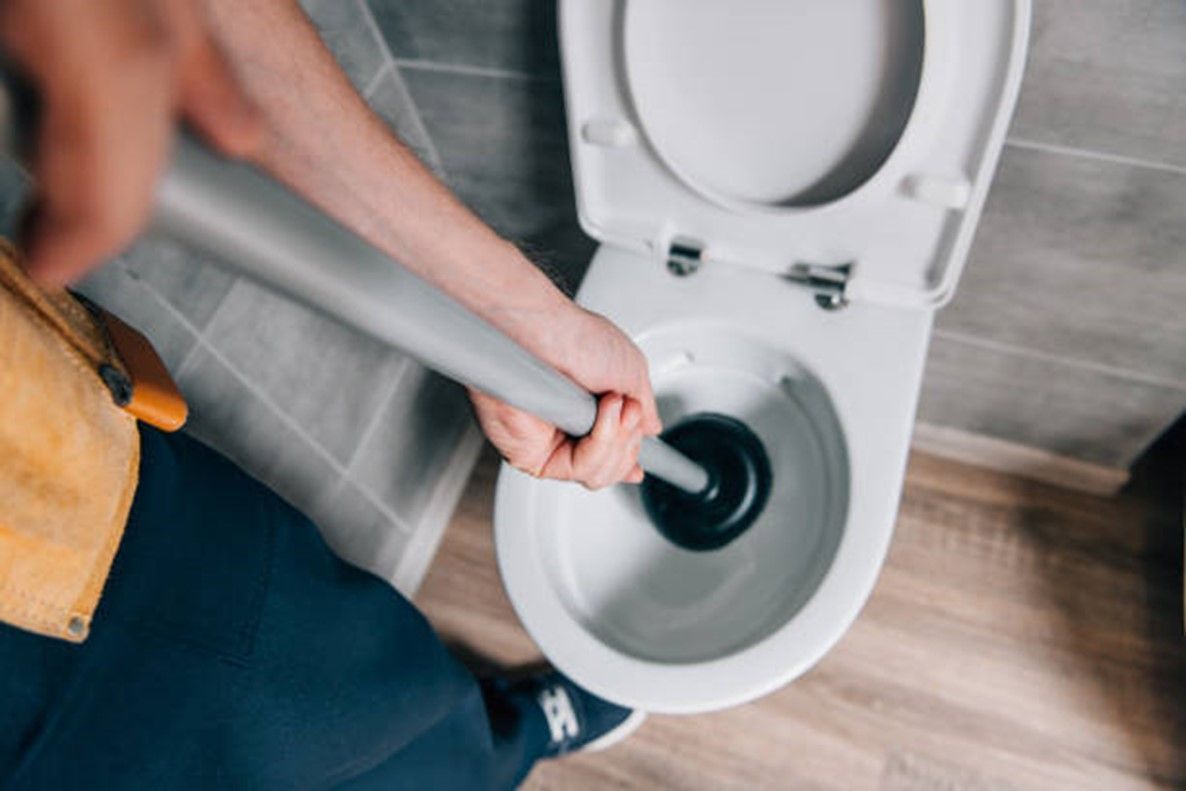 A person is using a plunger to unblock a toilet.