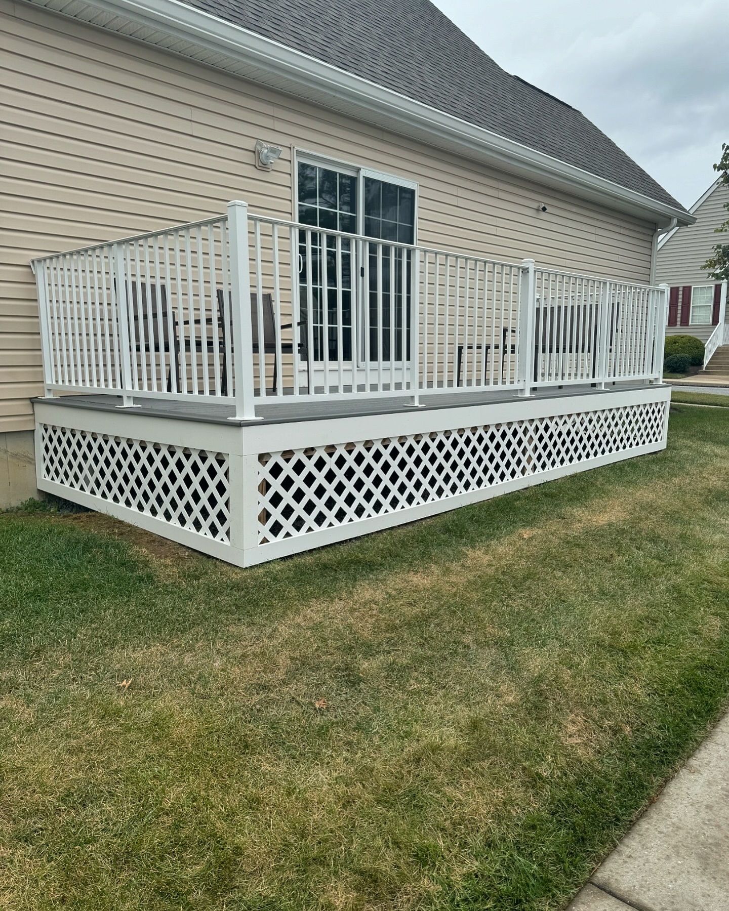 White deck with latticework and railing, beside a house with sliding glass doors.