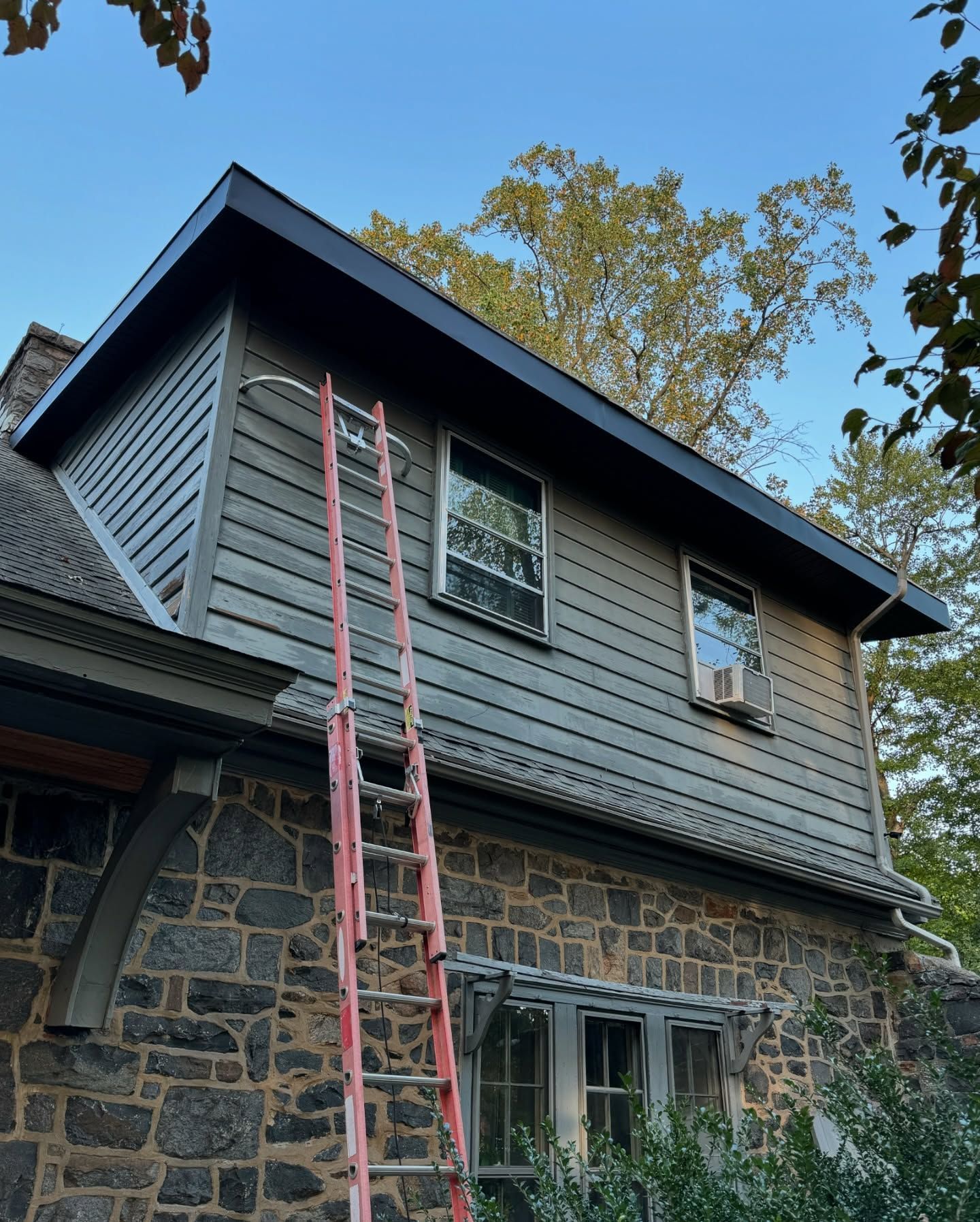 Exterior of a stone house with gray siding, black trim, and a red ladder leaning against the wall.