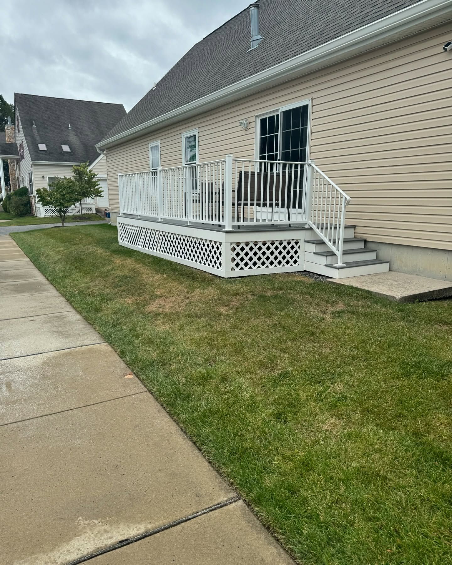 Deck with white railing and lattice work, steps, and sliding door on side of a house.