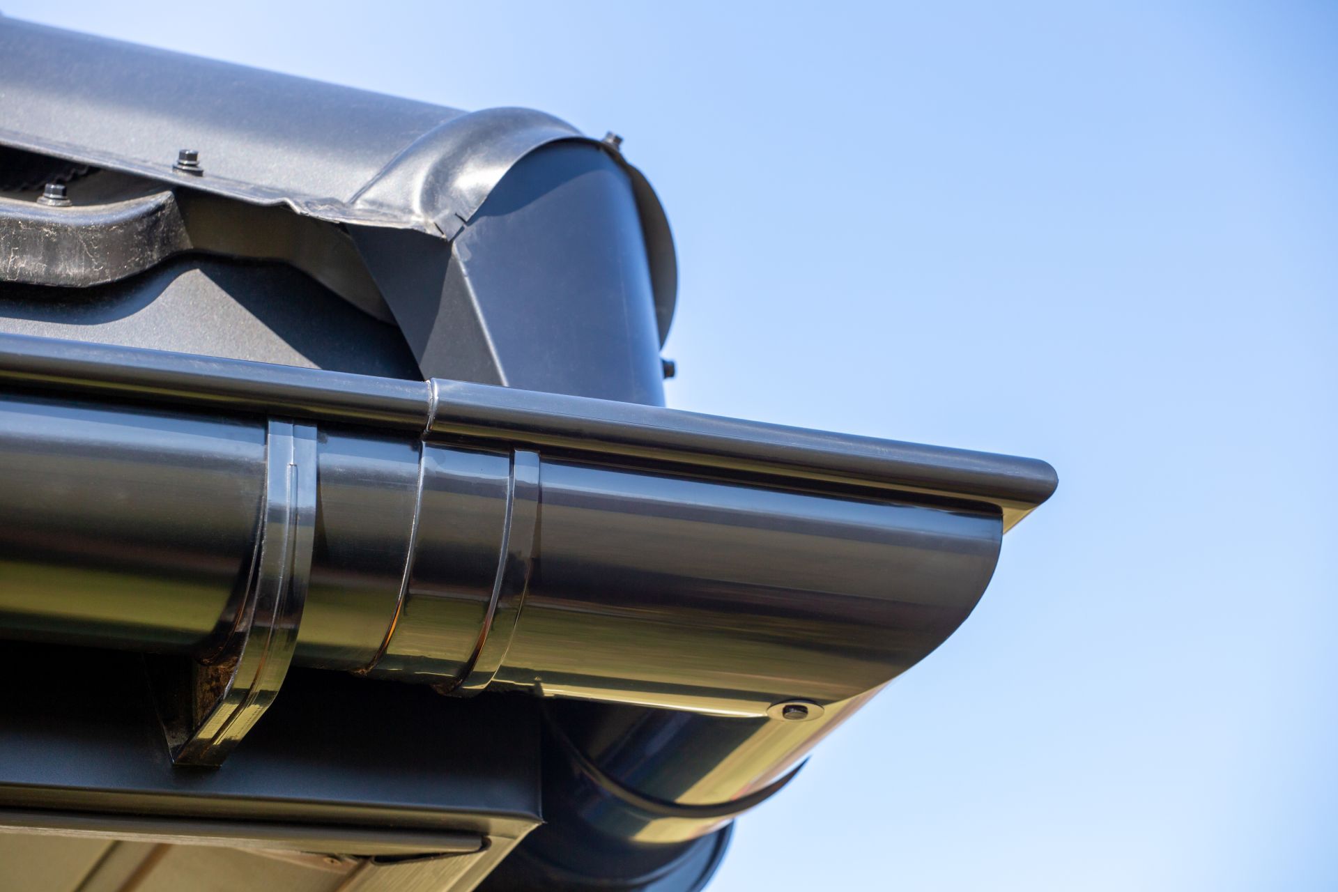 Dark gray rain gutter attached to a roof corner against a clear blue sky.