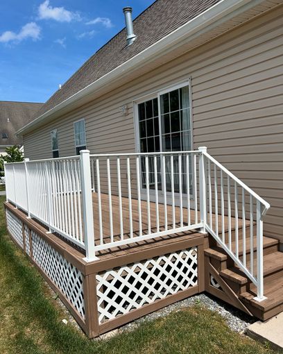Wooden deck with white railing, lattice skirting, and sliding glass door, against beige siding.